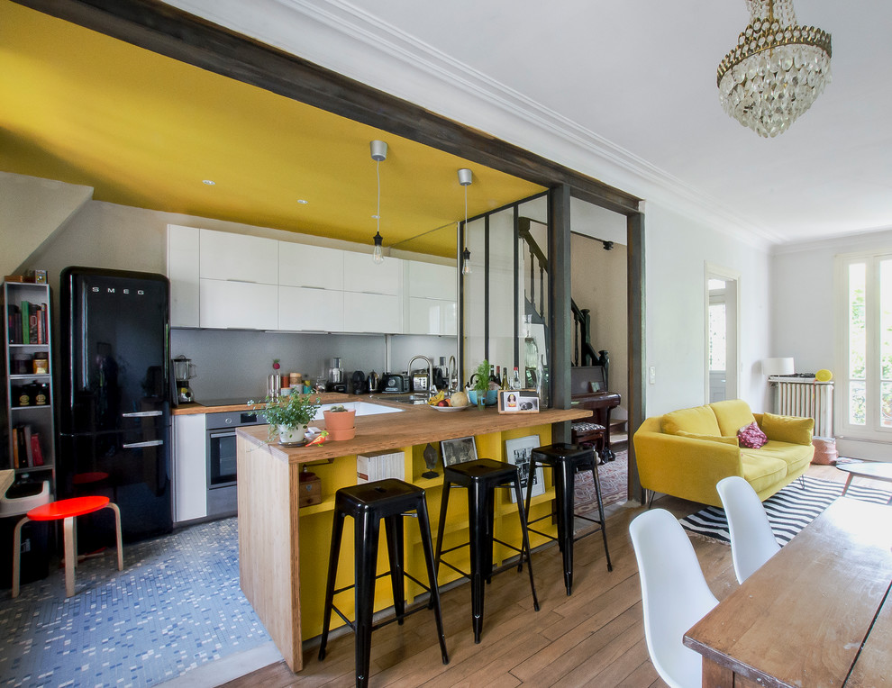 Small contemporary u-shaped open plan kitchen in Paris with a double-bowl sink, beaded inset cabinets, white cabinets, wood benchtops, grey splashback, metal splashback, black appliances, cement tiles, with island and multi-coloured floor.