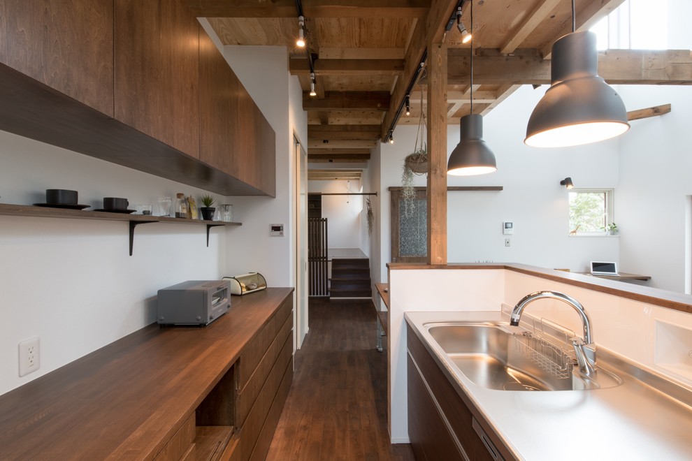 This is an example of a mid-sized asian galley eat-in kitchen in Sapporo with dark wood cabinets, stainless steel benchtops, dark hardwood floors, flat-panel cabinets, a peninsula, an integrated sink, white splashback and black appliances.