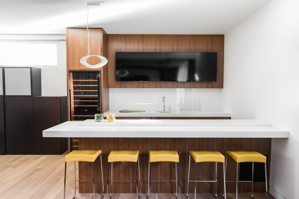 This is an example of a large modern galley wet bar in Calgary with light hardwood floors, an undermount sink, flat-panel cabinets, medium wood cabinets, quartzite benchtops, white splashback and glass sheet splashback.