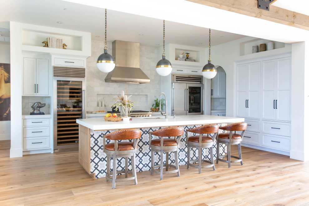 Example of a transitional l-shaped medium tone wood floor and brown floor open concept kitchen design with an undermount sink, shaker cabinets, white cabinets, stainless steel appliances, an island and white countertops