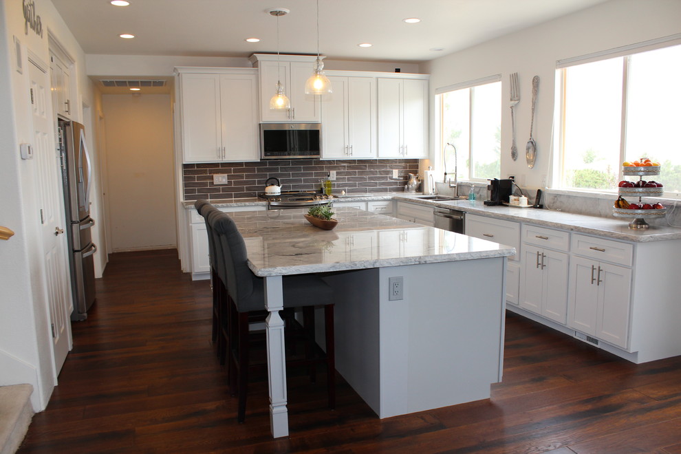 Mid-sized transitional l-shaped medium tone wood floor and brown floor open concept kitchen photo with an undermount sink, marble countertops, gray backsplash, ceramic backsplash, stainless steel appliances and an island