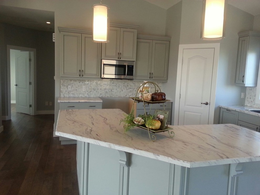 Photo of a mid-sized transitional l-shaped eat-in kitchen in Calgary with raised-panel cabinets, grey cabinets, laminate benchtops, stainless steel appliances, with island, a drop-in sink, grey splashback, ceramic splashback and vinyl floors.