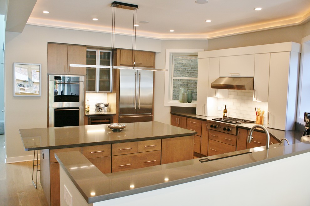 Inspiration for a large transitional u-shaped light wood floor kitchen remodel with an undermount sink, flat-panel cabinets, medium tone wood cabinets, quartz countertops, white backsplash, subway tile backsplash, stainless steel appliances and an island
