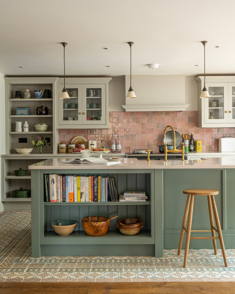 Photo of a traditional eat-in kitchen in Buckinghamshire with a farmhouse sink, shaker cabinets, green cabinets, solid surface benchtops, pink splashback, ceramic splashback, black appliances, ceramic floors, with island and white benchtop.