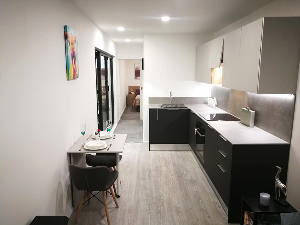 This is an example of a small contemporary l-shaped open plan kitchen in Other with an integrated sink, flat-panel cabinets, grey cabinets, laminate benchtops, grey splashback, panelled appliances, vinyl floors, no island, grey floor and grey benchtop.