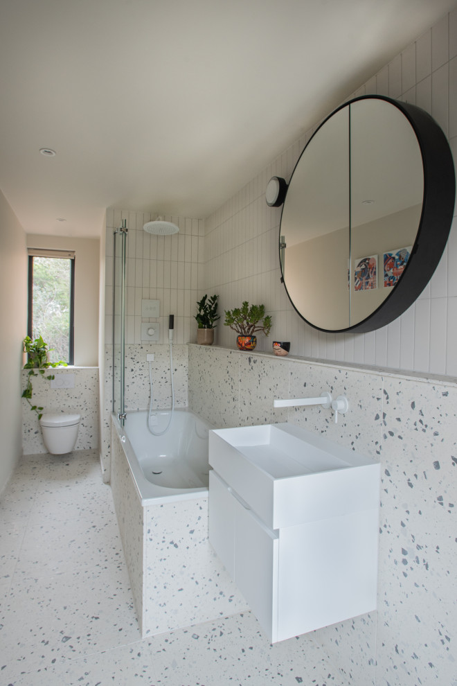 Inspiration for a small scandi family bathroom in London with flat-panel cabinets, white cabinets, a built-in bath, a shower/bath combination, a wall mounted toilet, white tiles, porcelain tiles, white walls, porcelain flooring, a wall-mounted sink, tiled worktops, white floors, white worktops, a single sink and a floating vanity unit.