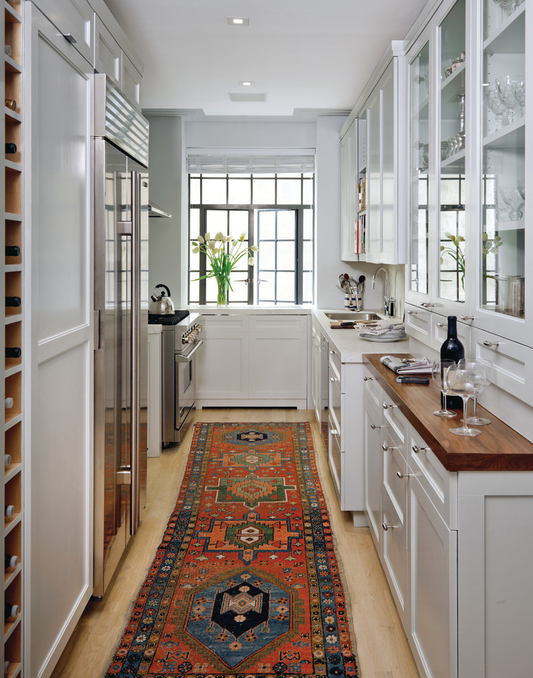 This is an example of a transitional u-shaped separate kitchen in New York with stainless steel appliances, glass-front cabinets, white cabinets and an undermount sink.