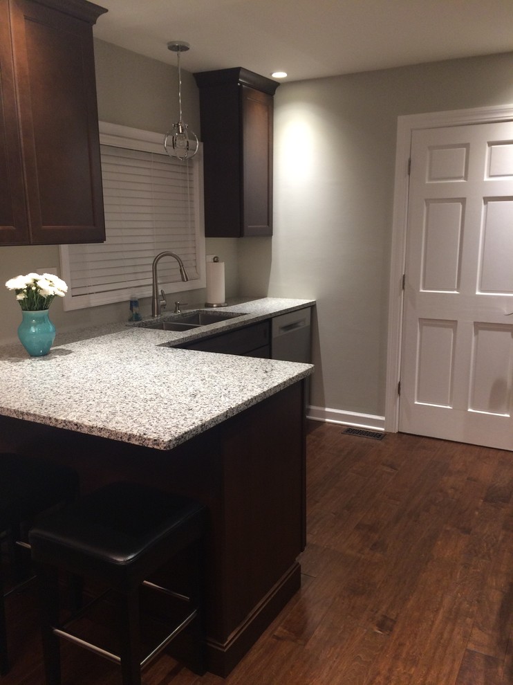 Inspiration for a large transitional l-shaped dark wood floor and brown floor eat-in kitchen remodel in Chicago with a double-bowl sink, recessed-panel cabinets, dark wood cabinets, granite countertops, white backsplash, stainless steel appliances, a peninsula and white countertops