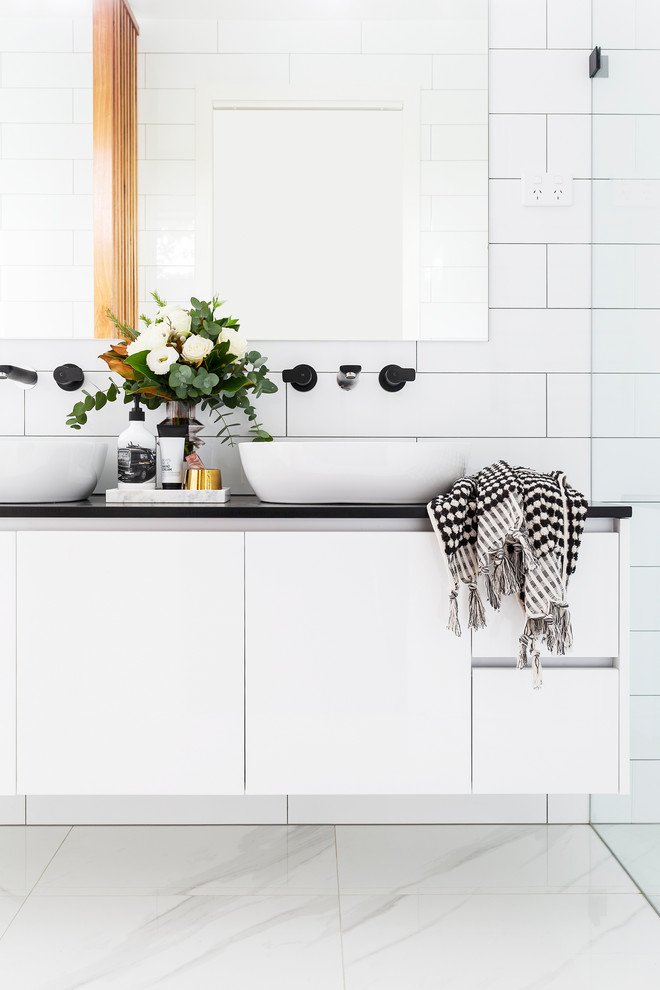 Design ideas for a mid-sized modern master bathroom in Canberra - Queanbeyan with furniture-like cabinets, white cabinets, a freestanding tub, an open shower, a one-piece toilet, white tile, subway tile, white walls, porcelain floors, a vessel sink, engineered quartz benchtops, white floor, an open shower and black benchtops.