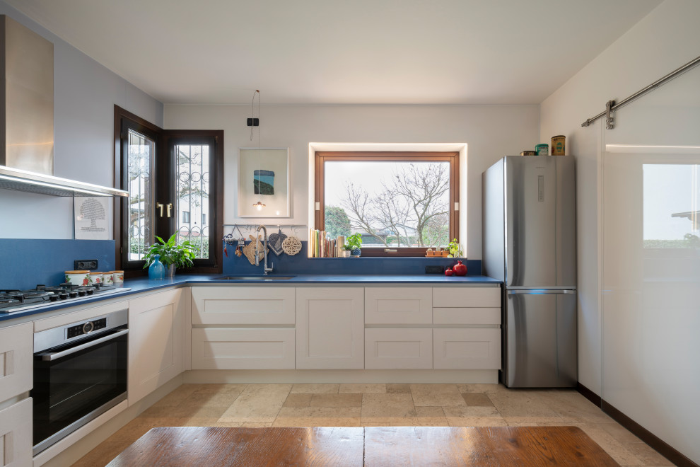 Foto på ett avskilt, mellanstort vintage blå l-kök, med en nedsänkt diskho, luckor med infälld panel, vita skåp, marmorbänkskiva, blått stänkskydd, stänkskydd i marmor, rostfria vitvaror, marmorgolv och beiget golv