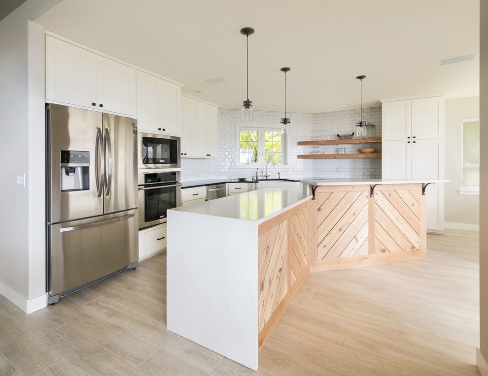 Photo of a large country eat-in kitchen in Other with a farmhouse sink, recessed-panel cabinets, white cabinets, quartz benchtops, white splashback, subway tile splashback, stainless steel appliances, light hardwood floors and with island.