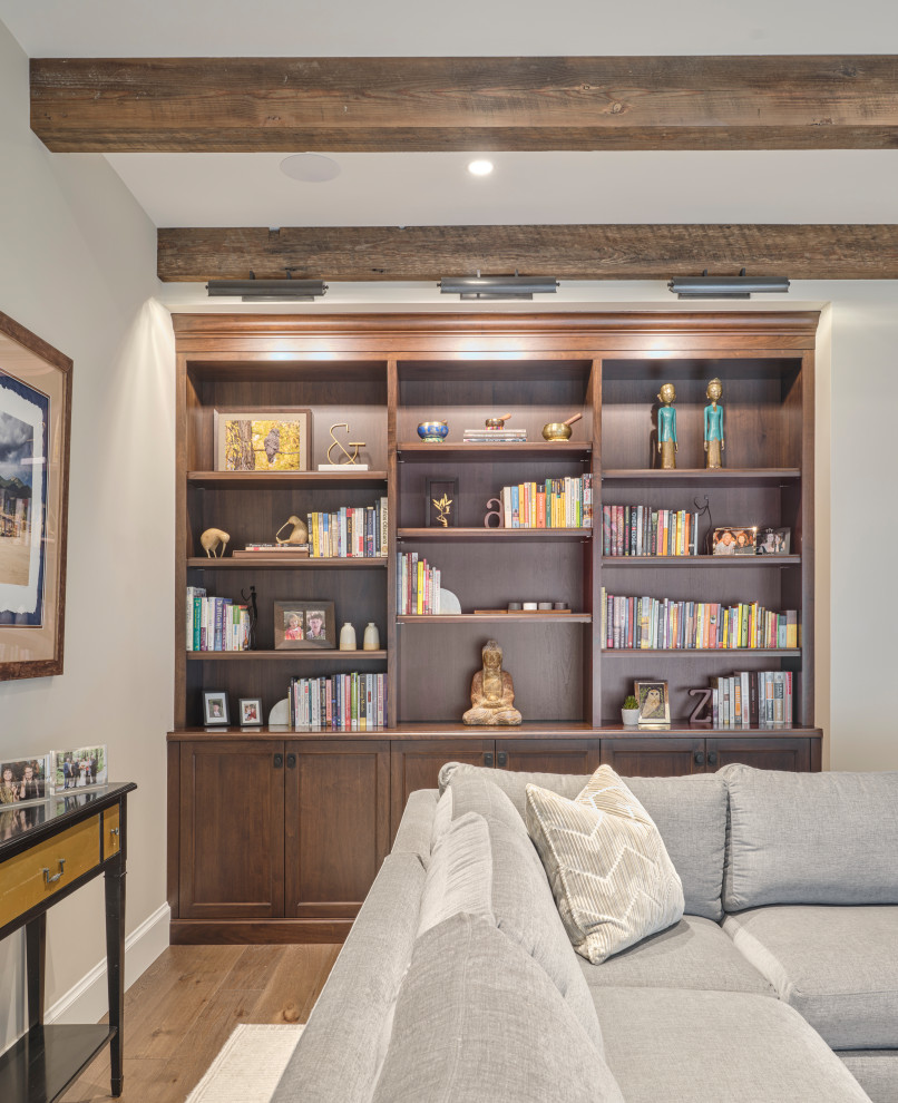 Modelo de sala de estar con biblioteca cerrada campestre de tamaño medio con paredes beige, suelo de madera en tonos medios, suelo beige y vigas vistas