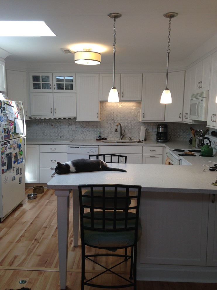 Mid-sized beach style l-shaped eat-in kitchen photo with an undermount sink, beaded inset cabinets, white cabinets, solid surface countertops, gray backsplash, mosaic tile backsplash, white appliances and a peninsula