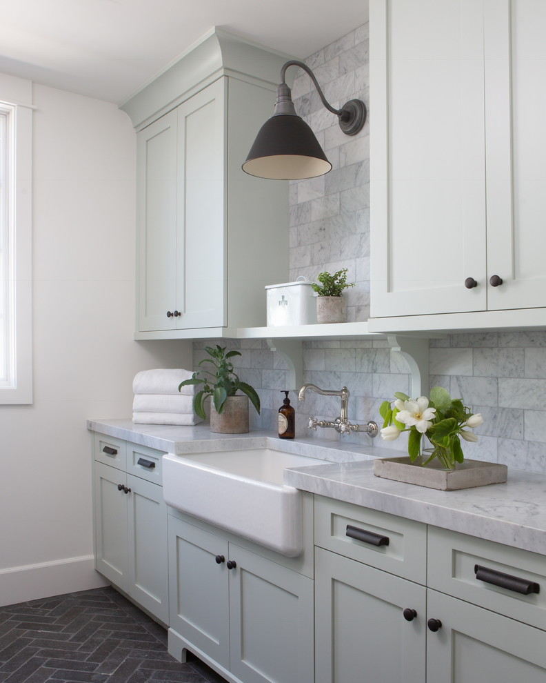 Photo of a large country galley dedicated laundry room in Phoenix with a farmhouse sink, shaker cabinets, green cabinets, marble benchtops, white walls, brick floors, a side-by-side washer and dryer, black floor and grey benchtop.