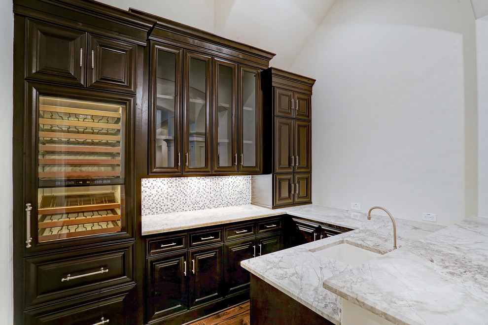This is an example of a mid-sized traditional home bar in Houston with an undermount sink, raised-panel cabinets, brown cabinets, granite benchtops, multi-coloured splashback, mosaic tile splashback, medium hardwood floors and brown floor.
