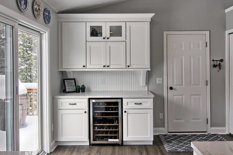 Mid-sized transitional l-shaped vinyl floor eat-in kitchen photo with a farmhouse sink, shaker cabinets, white cabinets, quartz countertops, white backsplash, stone tile backsplash, stainless steel appliances and an island