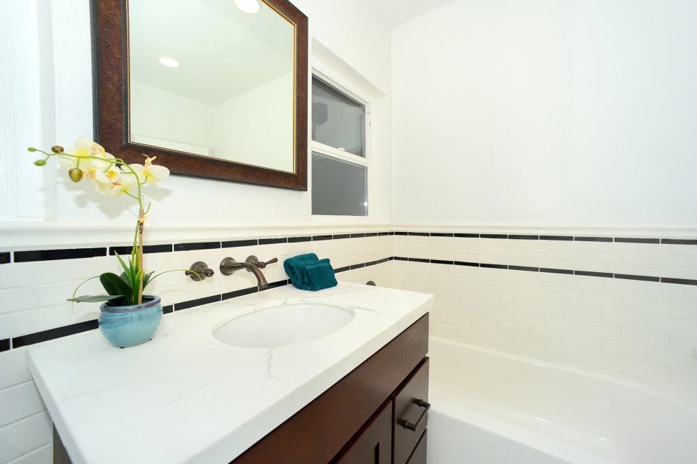 This is an example of a large traditional master bathroom in Los Angeles with shaker cabinets, brown cabinets, a corner tub, a double shower, a one-piece toilet, white tile, subway tile, white walls, porcelain floors, a drop-in sink, marble benchtops, white floor, a hinged shower door, white benchtops, a single vanity and a built-in vanity.