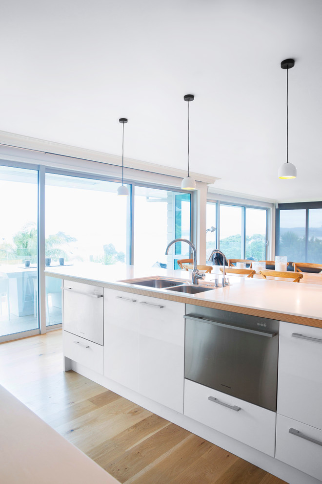 Mid-sized scandinavian u-shaped eat-in kitchen in Auckland with a double-bowl sink, flat-panel cabinets, white cabinets, blue splashback, ceramic splashback, stainless steel appliances, light hardwood floors and with island.
