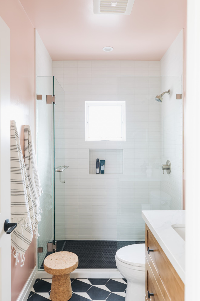 Design ideas for a small modern kids bathroom in San Francisco with shaker cabinets, medium wood cabinets, an alcove shower, a two-piece toilet, white tile, subway tile, pink walls, cement tiles, an undermount sink, engineered quartz benchtops, black floor, a hinged shower door, white benchtops, a single vanity and a built-in vanity.