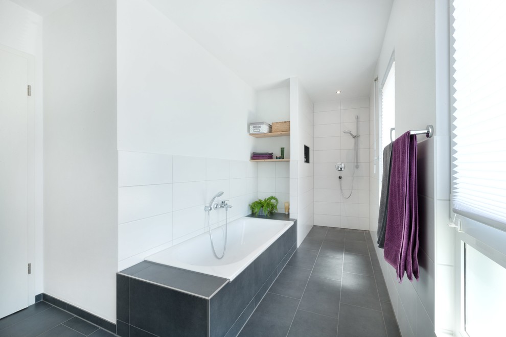 This is an example of a mid-sized contemporary 3/4 bathroom in Stuttgart with open cabinets, a drop-in tub, a curbless shower, white tile, ceramic tile, white walls, ceramic floors, black floor and an open shower.