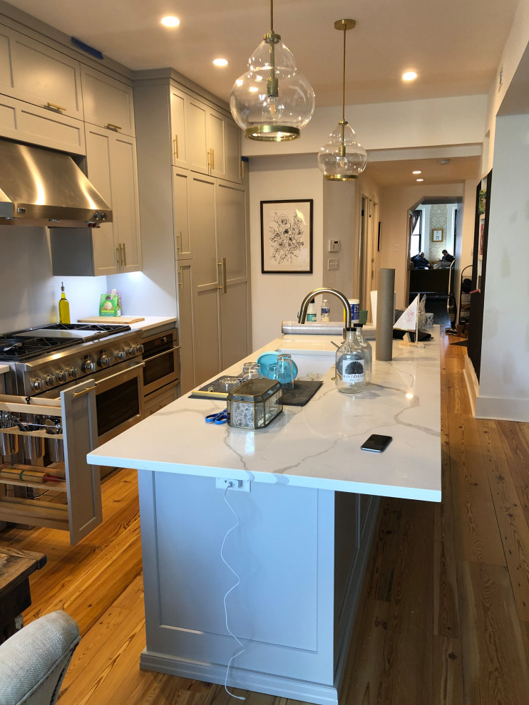 Photo of a medium sized classic single-wall kitchen/diner in Philadelphia with a submerged sink, shaker cabinets, grey cabinets, engineered stone countertops, white splashback, stainless steel appliances, medium hardwood flooring, an island, yellow floors and white worktops.