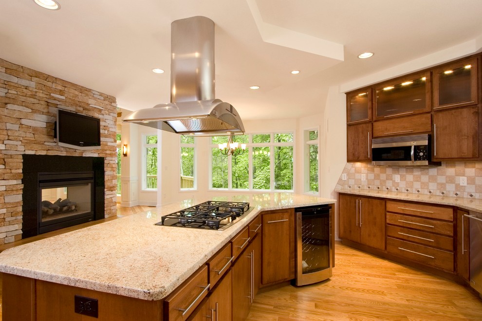 Eat-in kitchen - large transitional galley light wood floor eat-in kitchen idea with flat-panel cabinets, medium tone wood cabinets, granite countertops, beige backsplash, ceramic backsplash, stainless steel appliances and an island