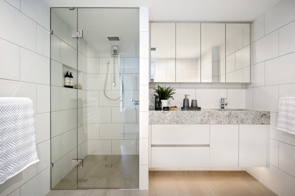 Mid-sized contemporary 3/4 bathroom in Gold Coast - Tweed with flat-panel cabinets, white cabinets, an alcove shower, white tile, an undermount sink, beige floor, a hinged shower door and grey benchtops.