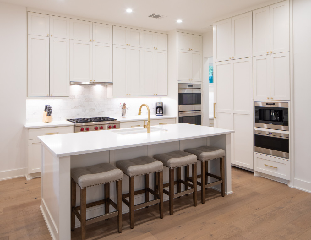 Eat-in kitchen - mid-sized transitional l-shaped light wood floor and brown floor eat-in kitchen idea in Austin with an undermount sink, shaker cabinets, white cabinets, quartz countertops, white backsplash, marble backsplash, stainless steel appliances, an island and white countertops