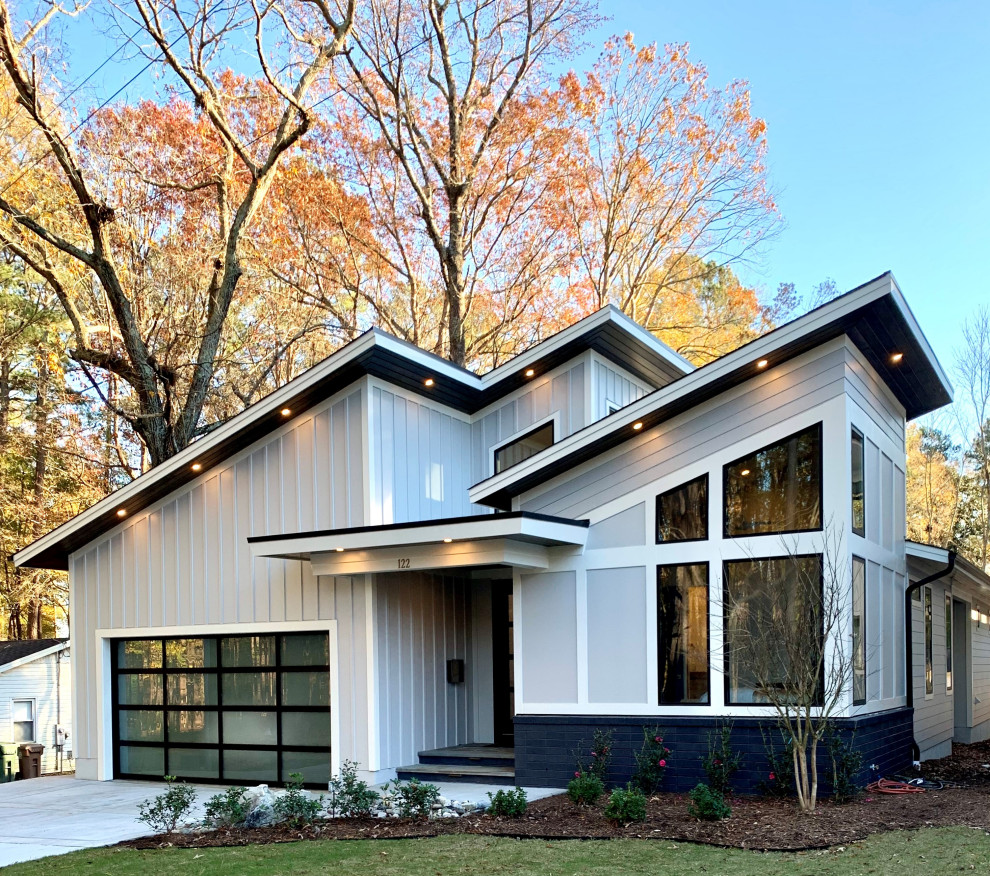 Medium sized and gey contemporary bungalow detached house in Raleigh with wood cladding, a lean-to roof, a shingle roof, a black roof and board and batten cladding.