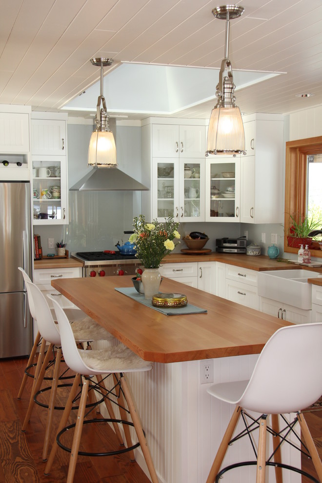Mid-sized country l-shaped kitchen in Vancouver with a farmhouse sink, shaker cabinets, white cabinets, wood benchtops, blue splashback, glass sheet splashback, stainless steel appliances and medium hardwood floors.