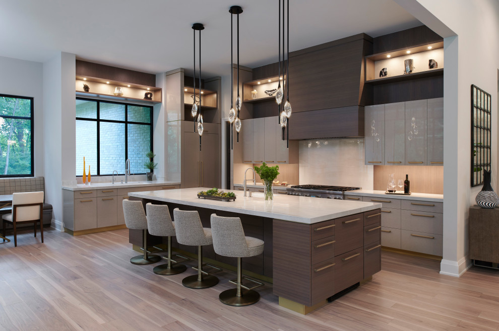 Photo of a large contemporary single-wall kitchen/diner in Detroit with a submerged sink, flat-panel cabinets, beige cabinets, quartz worktops, beige splashback, porcelain splashback, stainless steel appliances, light hardwood flooring, an island, brown floors and white worktops.