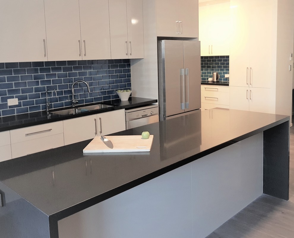 Photo of a large modern galley kitchen pantry in Brisbane with a double-bowl sink, flat-panel cabinets, white cabinets, quartz benchtops, blue splashback, subway tile splashback, stainless steel appliances, with island and black benchtop.