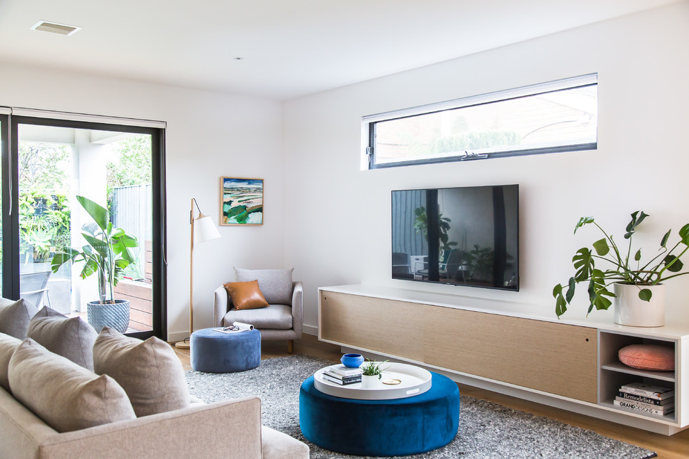 This is an example of a large contemporary formal enclosed living room in Melbourne with white walls, light hardwood floors, a wall-mounted tv and beige floor.