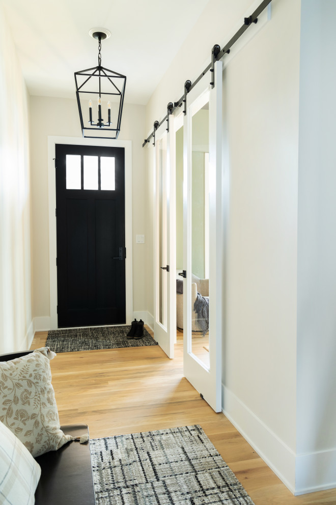 Стильный дизайн: фойе в стиле неоклассика (современная классика) с белыми стенами, светлым паркетным полом, одностворчатой входной дверью, черной входной дверью и коричневым полом - последний тренд