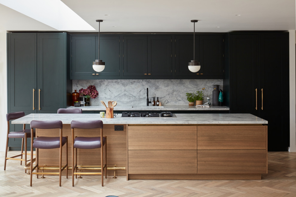 This is an example of an expansive transitional open plan kitchen in London with shaker cabinets, green cabinets, granite benchtops, grey splashback, granite splashback, medium hardwood floors, with island and grey benchtop.