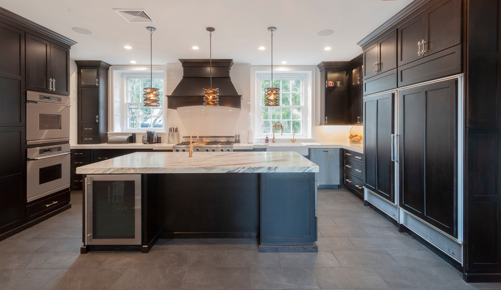 Large transitional u-shaped eat-in kitchen in Philadelphia with a farmhouse sink, shaker cabinets, black cabinets, marble benchtops, white splashback, subway tile splashback, stainless steel appliances, porcelain floors, with island, black floor and white benchtop.