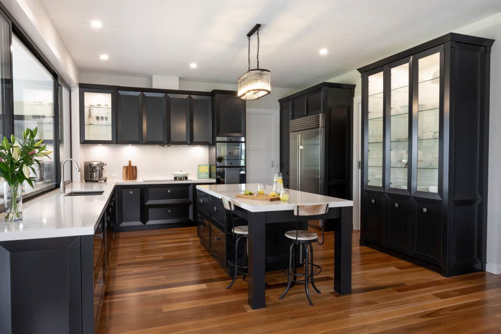 This is an example of an expansive transitional u-shaped kitchen in Other with an undermount sink, recessed-panel cabinets, black cabinets, window splashback, with island, brown floor and white benchtop.