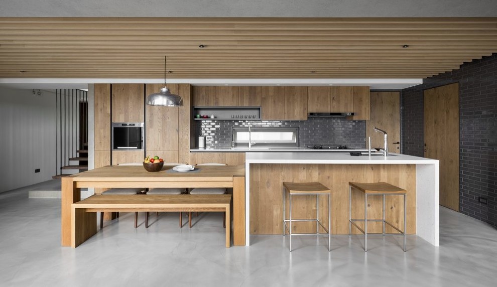 This is an example of a mid-sized contemporary galley open plan kitchen in Barcelona with light wood cabinets, quartz benchtops, stainless steel appliances, concrete floors, with island, grey floor, an undermount sink, flat-panel cabinets, grey splashback and subway tile splashback.