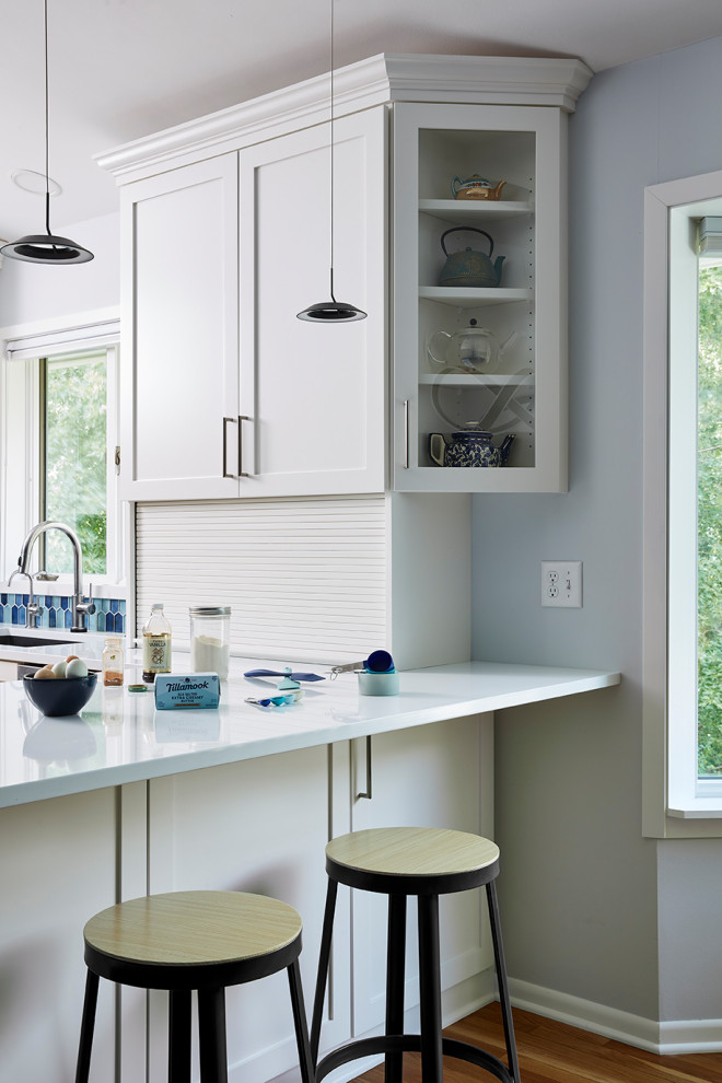 Modern inredning av ett stort vit vitt kök, med en undermonterad diskho, skåp i shakerstil, vita skåp, bänkskiva i kvarts, blått stänkskydd, stänkskydd i glaskakel, rostfria vitvaror, mellanmörkt trägolv, en halv köksö och brunt golv