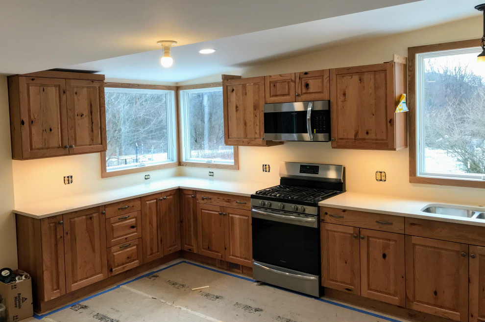 Mid-sized country l-shaped separate kitchen in New York with an undermount sink, raised-panel cabinets, medium wood cabinets, red splashback, stainless steel appliances, no island, beige floor and white benchtop.