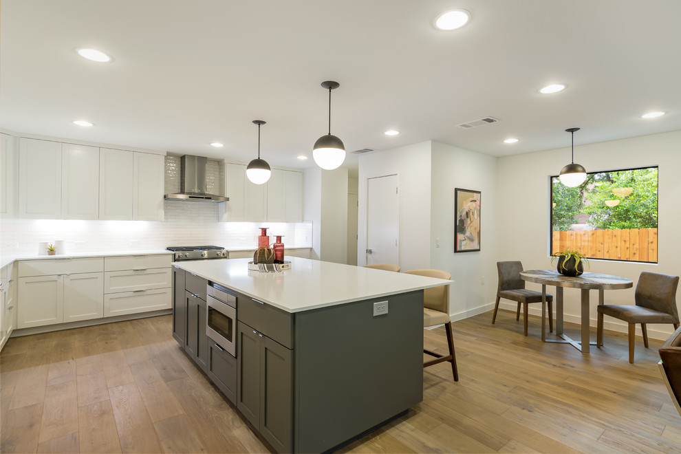 Inspiration for a mid-sized contemporary l-shaped open plan kitchen in Austin with an undermount sink, shaker cabinets, white cabinets, quartz benchtops, white splashback, subway tile splashback, stainless steel appliances, medium hardwood floors, with island, brown floor and white benchtop.