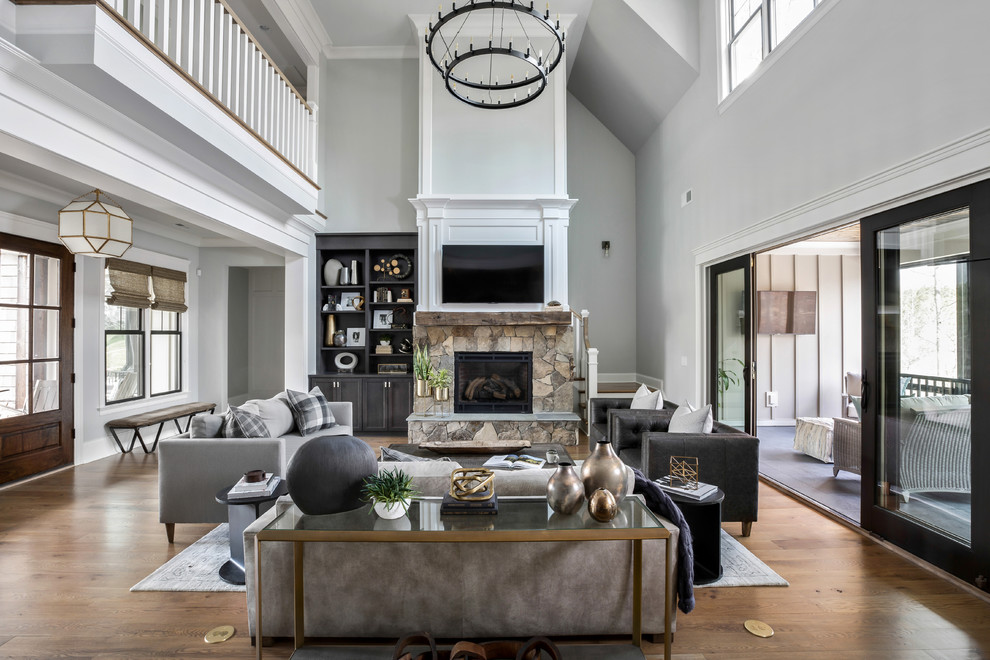 Transitional living room in Charlotte with grey walls, medium hardwood floors, a standard fireplace, a stone fireplace surround, a wall-mounted tv and brown floor.