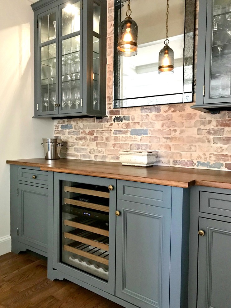 Mid-sized traditional single-wall wet bar in Philadelphia with no sink, recessed-panel cabinets, grey cabinets, wood benchtops, multi-coloured splashback, brick splashback, dark hardwood floors, brown floor and brown benchtop.
