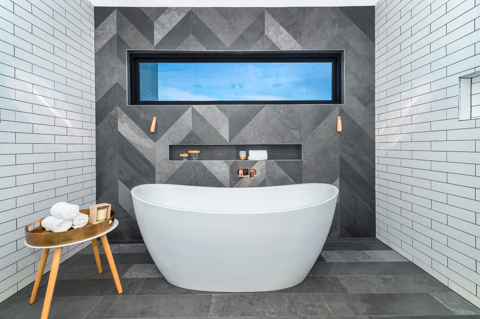 This is an example of a large contemporary master bathroom in Canberra - Queanbeyan with beaded inset cabinets, light wood cabinets, a freestanding tub, a double shower, a wall-mount toilet, gray tile, subway tile, white walls, ceramic floors, a vessel sink and wood benchtops.