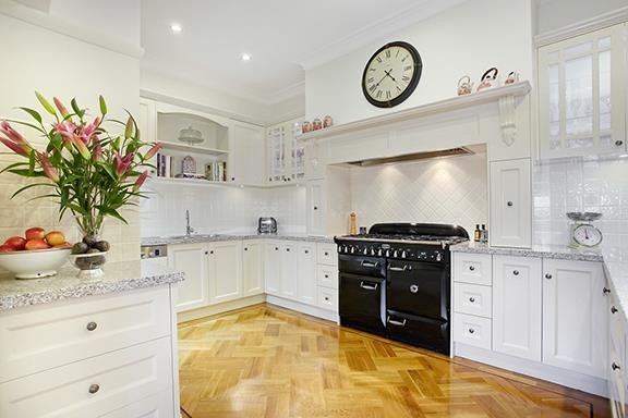 Inspiration for an expansive traditional u-shaped eat-in kitchen in Melbourne with a drop-in sink, recessed-panel cabinets, black cabinets, quartzite benchtops, black splashback, ceramic splashback, black appliances, light hardwood floors and no island.
