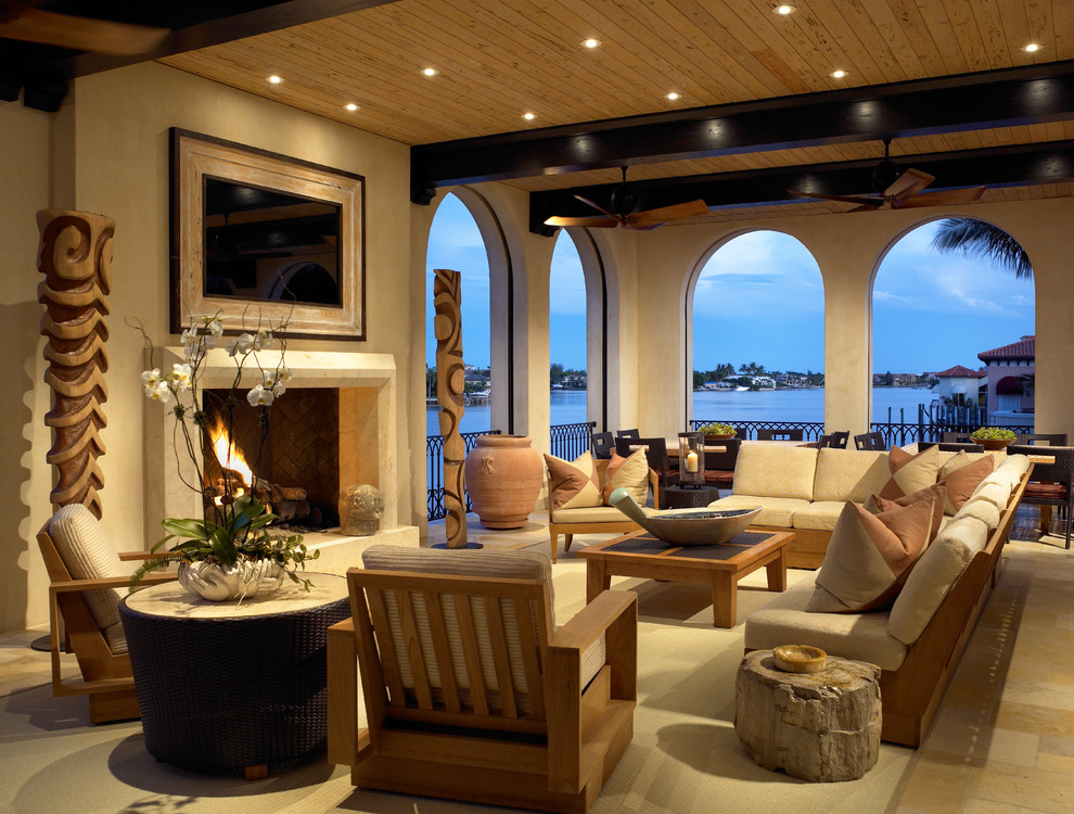 This is an example of a large tropical formal open concept living room in Miami with beige walls, ceramic floors, a standard fireplace, a stone fireplace surround and a wall-mounted tv.