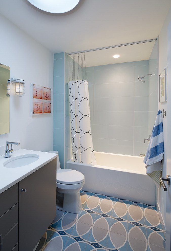 This is an example of a mid-sized midcentury kids bathroom in DC Metro with grey cabinets, an alcove tub, a shower/bathtub combo, a two-piece toilet, blue tile, gray tile, white tile, ceramic tile, white walls, ceramic floors, an undermount sink and engineered quartz benchtops.