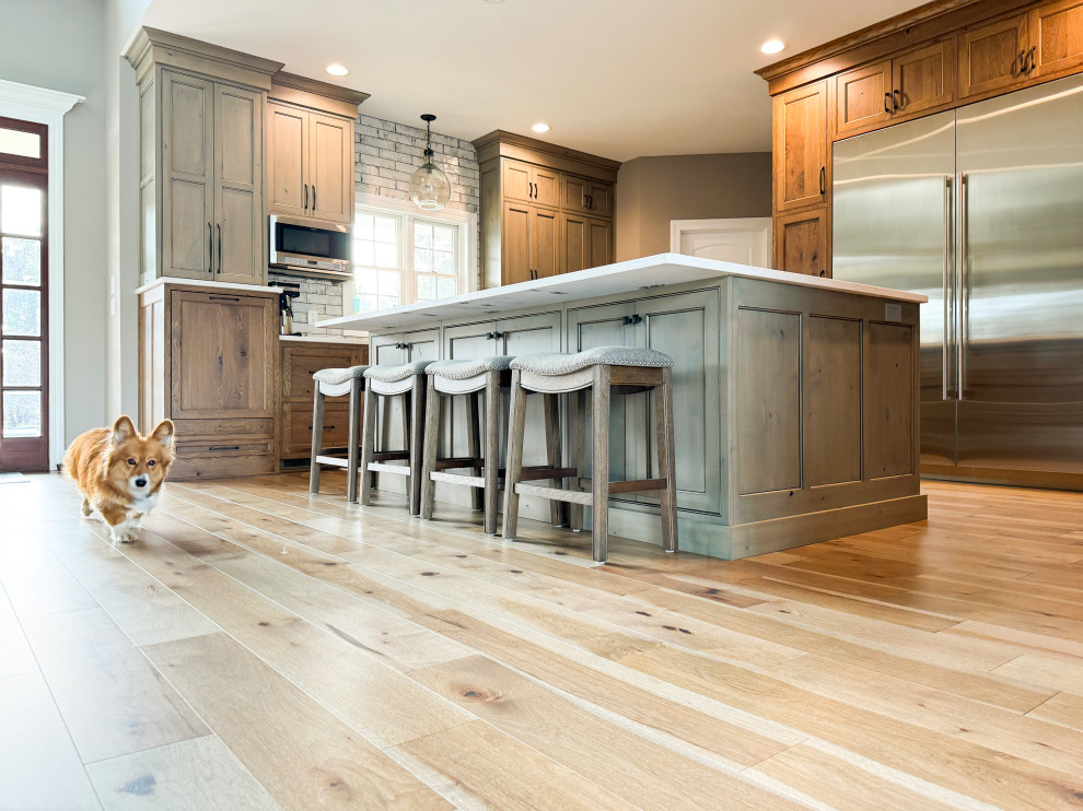 Example of a large transitional l-shaped light wood floor eat-in kitchen design with a farmhouse sink, beaded inset cabinets, quartz countertops, white backsplash, subway tile backsplash, stainless steel appliances and an island