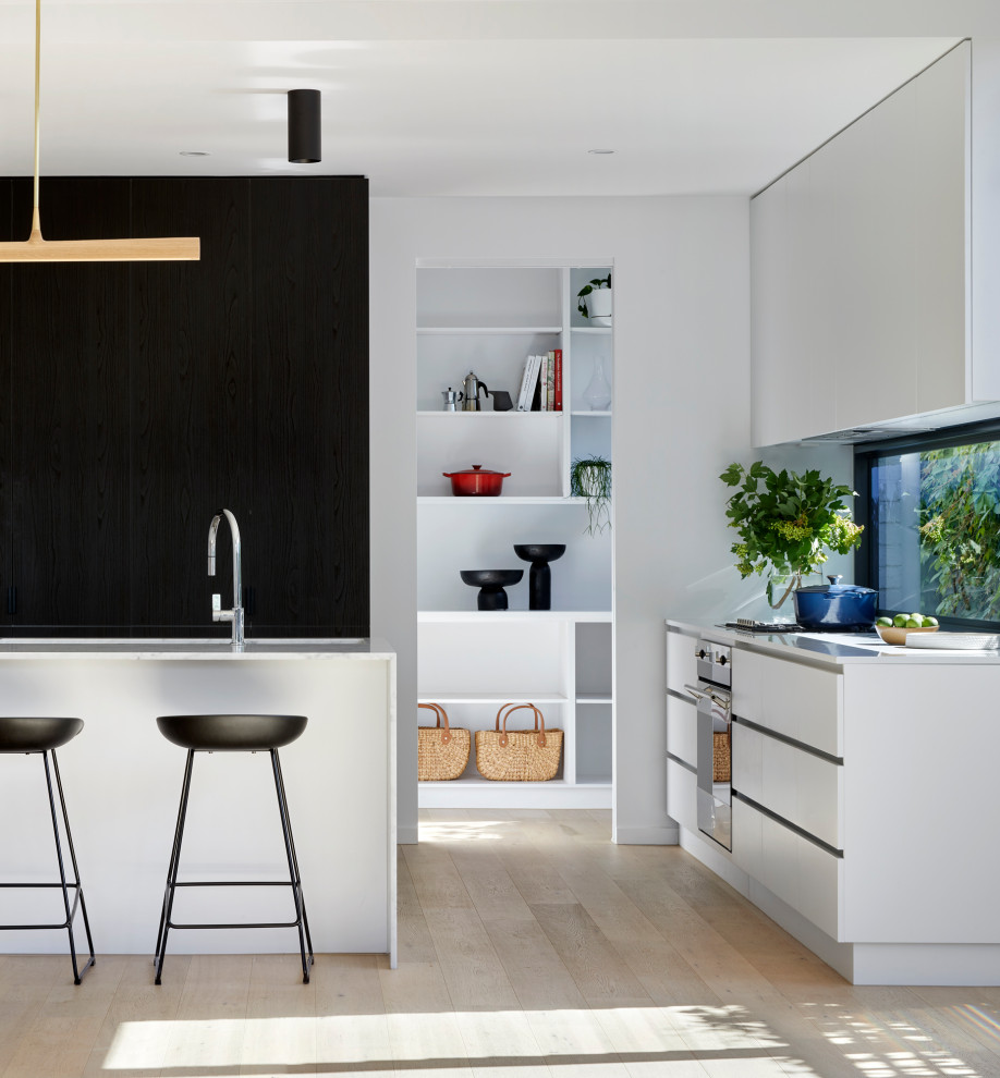 Moderne Küche mit Vorratsschrank, Unterbauwaschbecken, dunklen Holzschränken, Marmor-Arbeitsplatte, Glasrückwand, Küchengeräten aus Edelstahl, hellem Holzboden, Kücheninsel und weißer Arbeitsplatte in Melbourne