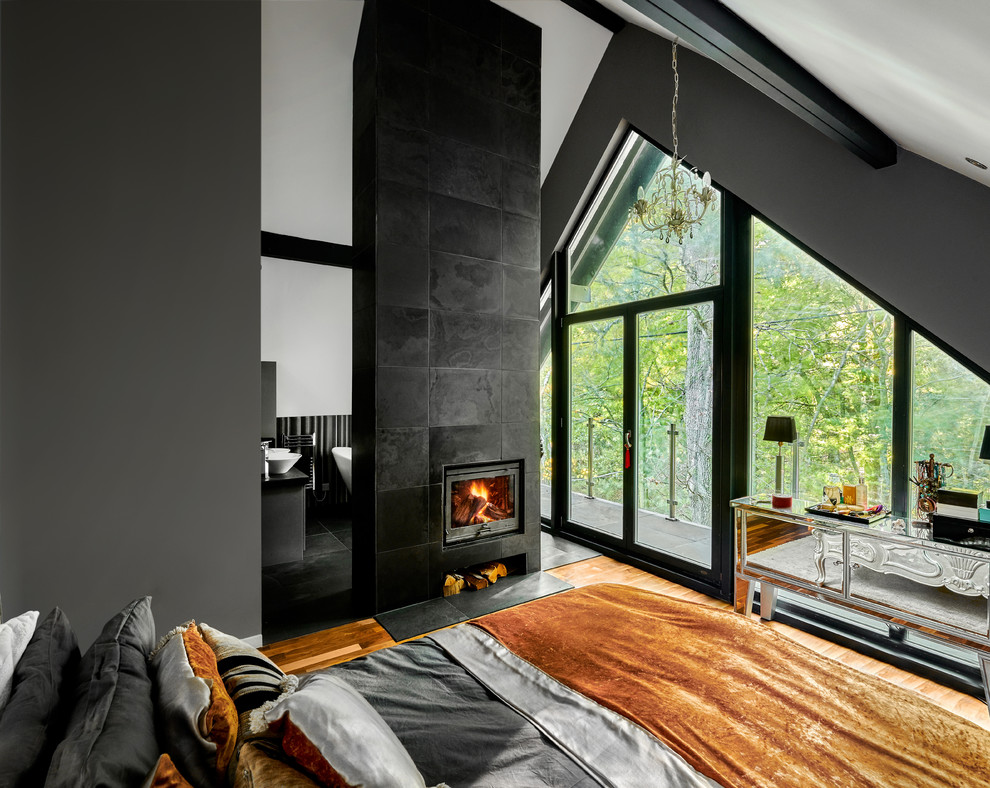 Mid-sized scandinavian master bedroom in Hampshire with grey walls, light hardwood floors, a wood stove, a tile fireplace surround and brown floor.